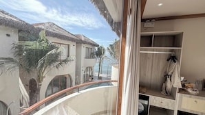 A balcony with a view of a building and palm trees, a wooden railing, and a room with a wardrobe and a small table. - La Mer Bali Mui Ne (Mui Ne)