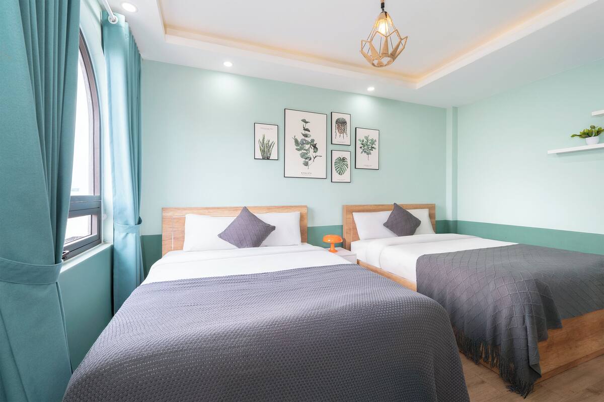 A room with two beds, teal walls, and framed botanical prints.