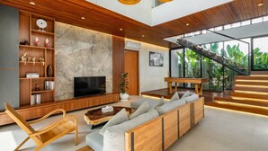 A modern living room with a wooden floor, a large TV, a sofa, and a staircase leading to an upper level. - De Dominique Villas Canggu (Canggu)
