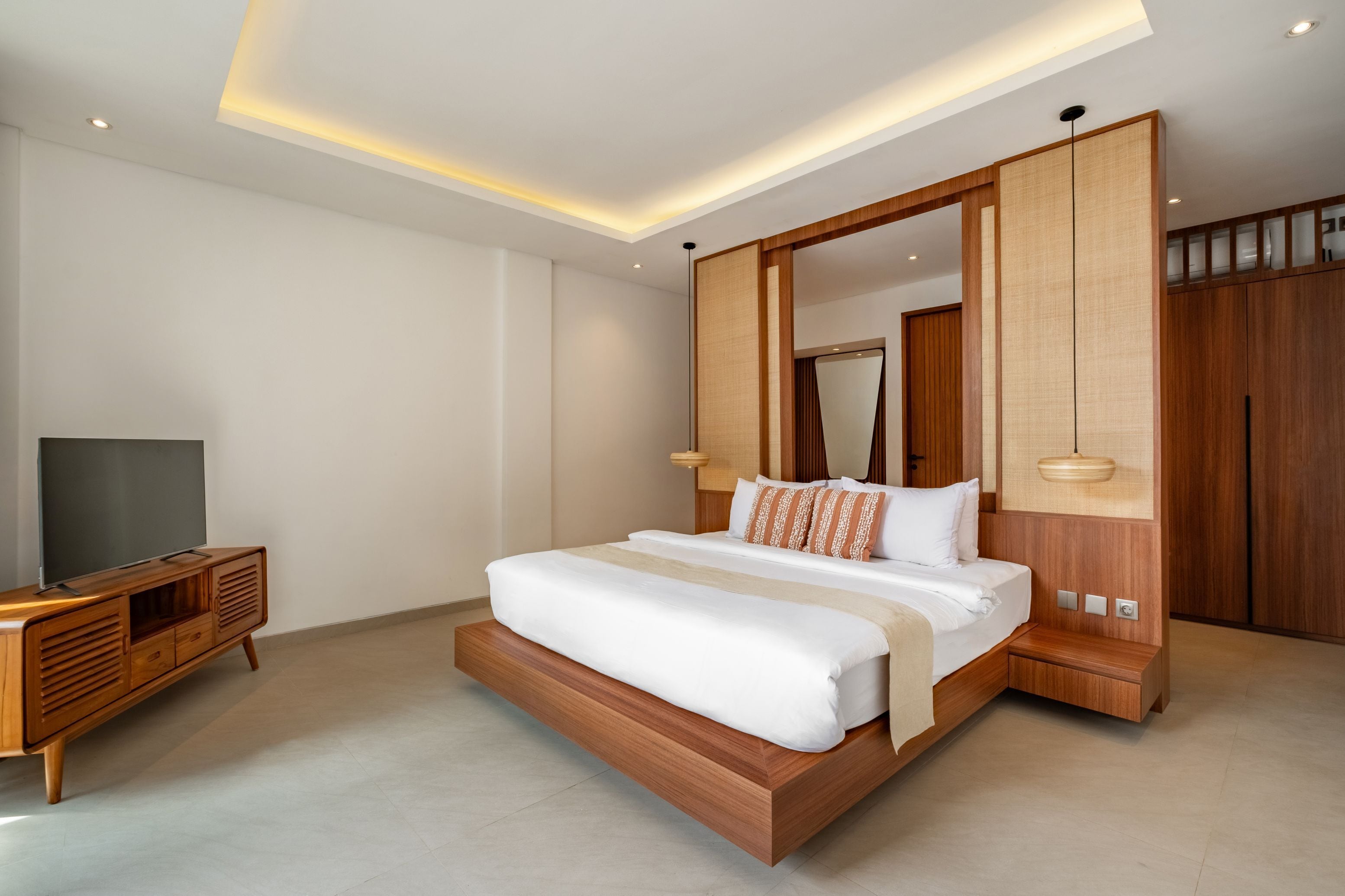 A modern bedroom with a large bed, wooden headboard, and a television on a wooden cabinet.