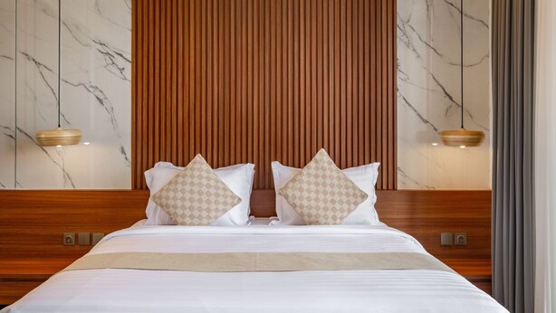 A hotel room with a wooden headboard, marble walls, and two bedside tables with lamps. - De Dominique Villas Canggu (Canggu)