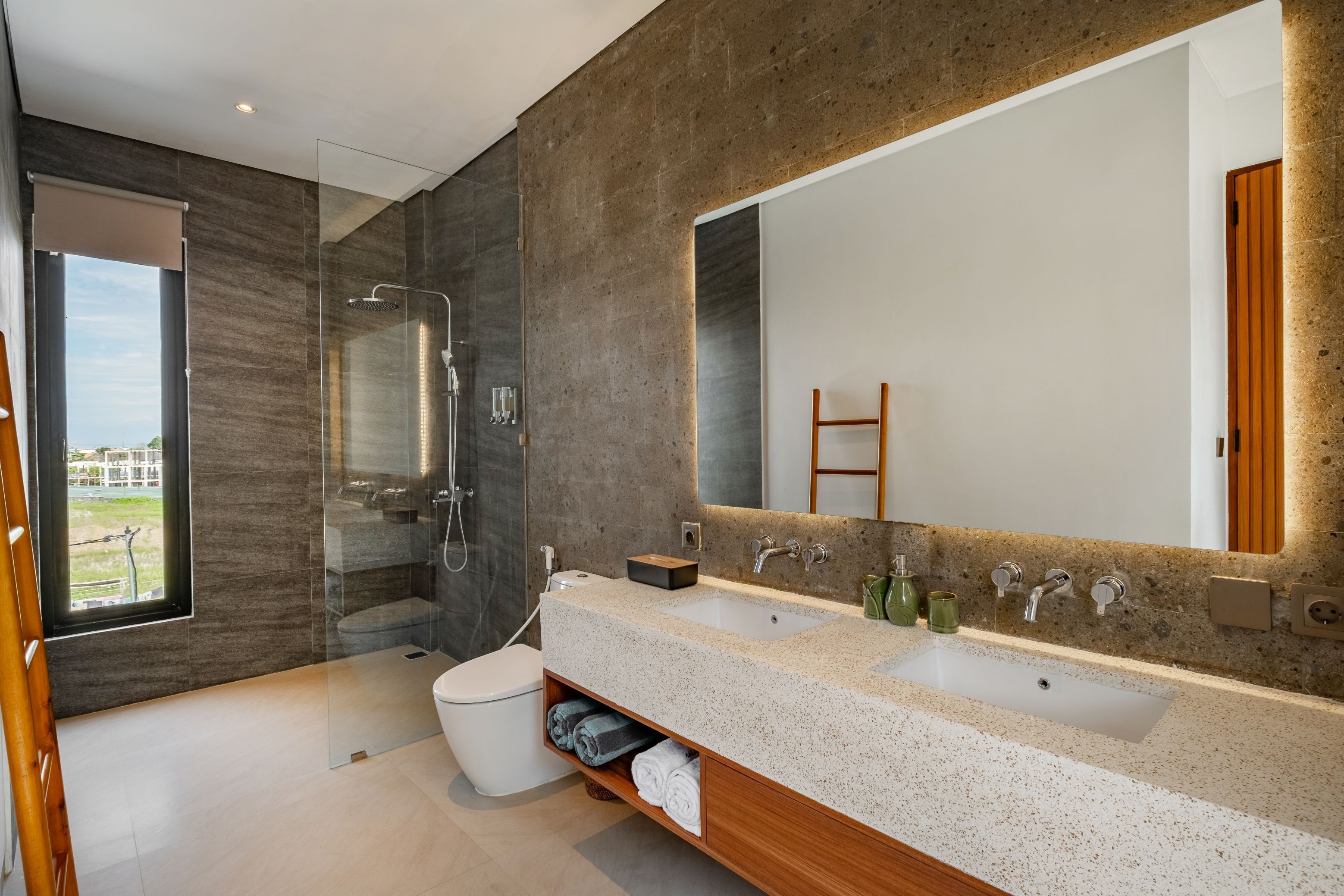 Een moderne badkamer met een grote spiegel, twee wastafels, een douche en een toilet.