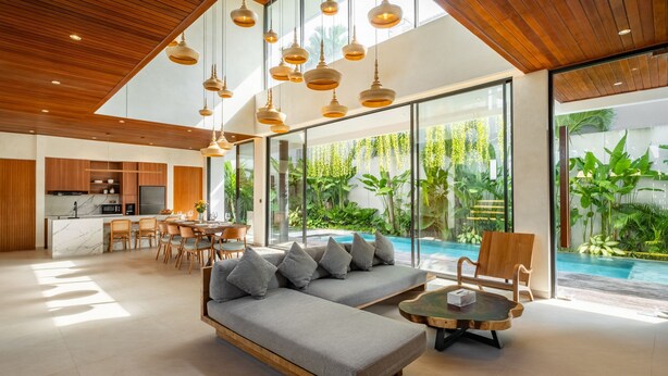 A modern living room with a sofa, dining area, and a view of a swimming pool. - De Dominique Villas Canggu (Canggu)
