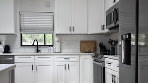 Eine moderne Küche mit weißen Schränken, einer eingebauten Mikrowelle und einem Edelstahl-Kühlschrank.