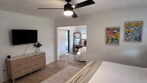 Ein modernes Schlafzimmer mit Bett, Fernseher, Deckenventilator, Schminktisch und Bildern an den Wänden.