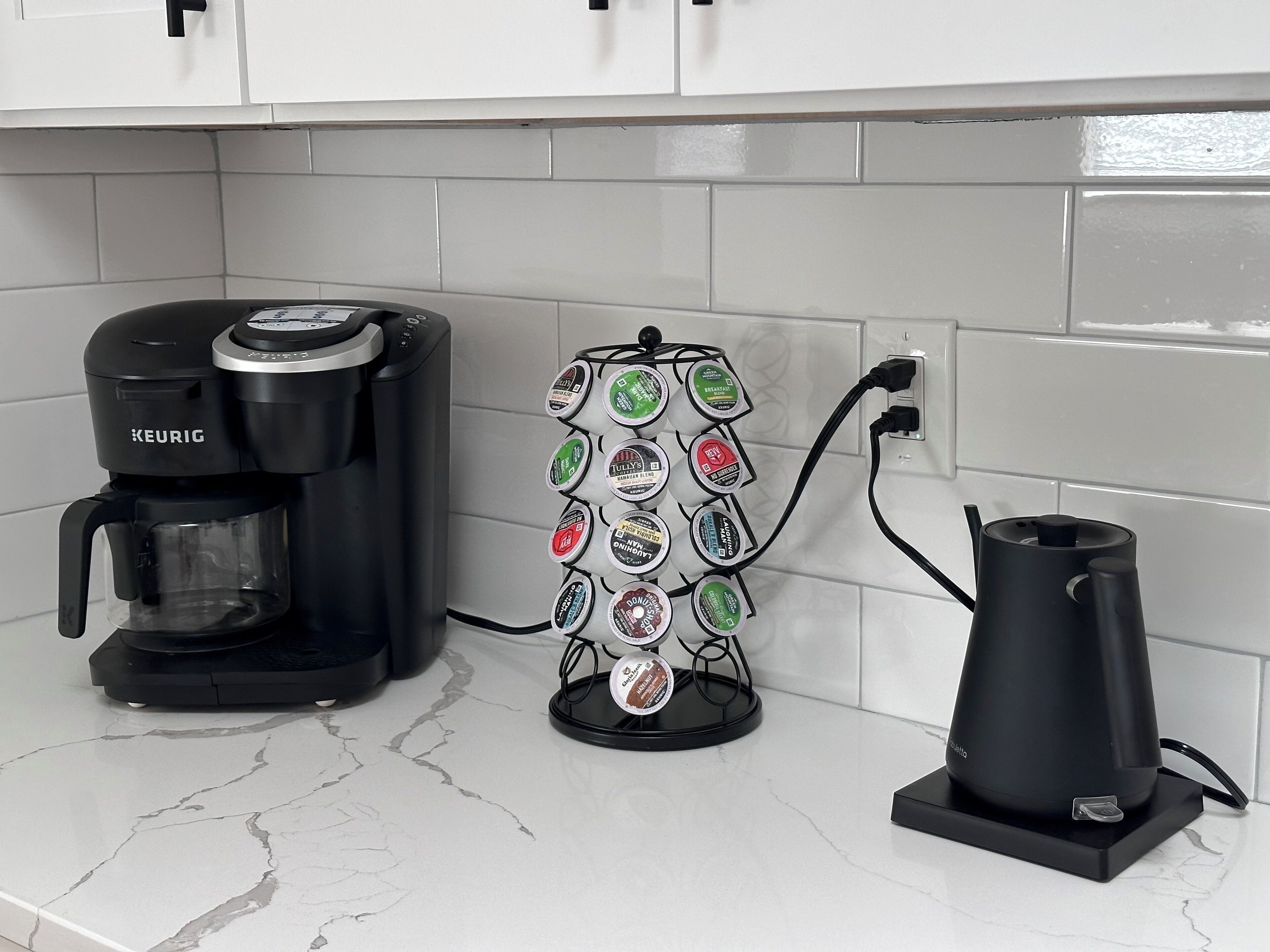 Uma cafeteira, um suporte para cápsulas de café e uma chaleira em uma bancada de cozinha.