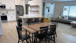 Eine moderne Küche mit weißen Schränken, einer zentralen Kochinsel und einem Essbereich mit einem Holztisch und schwarzen Stühlen.