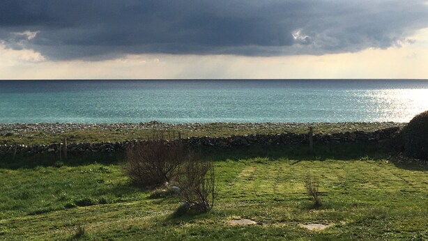 A coastal landscape with a grassy field, a stone wall, and a view of the sea under a cloudy sky. - Oceanfront Vacation – House with a Garden Right Next to the Beach (plozevet)