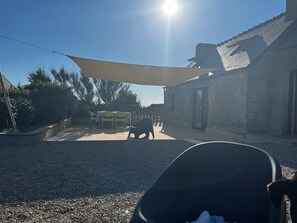 A patio area with a table and chairs, a shaded area, and a building with a sloped roof.