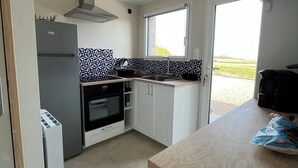 A compact kitchen with a built-in oven, a refrigerator, and a microwave. There is a window providing natural light and a view of the outdoors. - Oceanfront Vacation – House with a Garden Right Next to the Beach (plozevet)