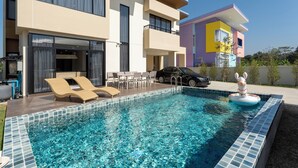 A modern pool area with lounge chairs, a car, and a colorful building in the background. - Kanna Farmhouse Pool Villa (Tambon San Phranet)