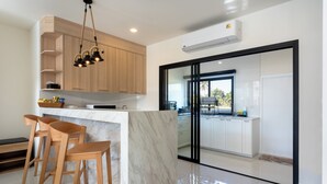 A modern kitchen with wooden cabinets, a marble island, and bar stools. - Kanna Farmhouse Pool Villa (Tambon San Phranet)