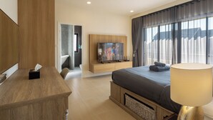 A modern hotel room with a wooden desk, a flat-screen TV mounted on the wall, a large bed with a grey duvet, and a window with curtains. - Kanna Farmhouse Pool Villa (Tambon San Phranet)