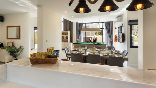 A modern dining area with a marble countertop, a pool table in the background, and pendant lighting. - Kanna Farmhouse Pool Villa (Tambon San Phranet)