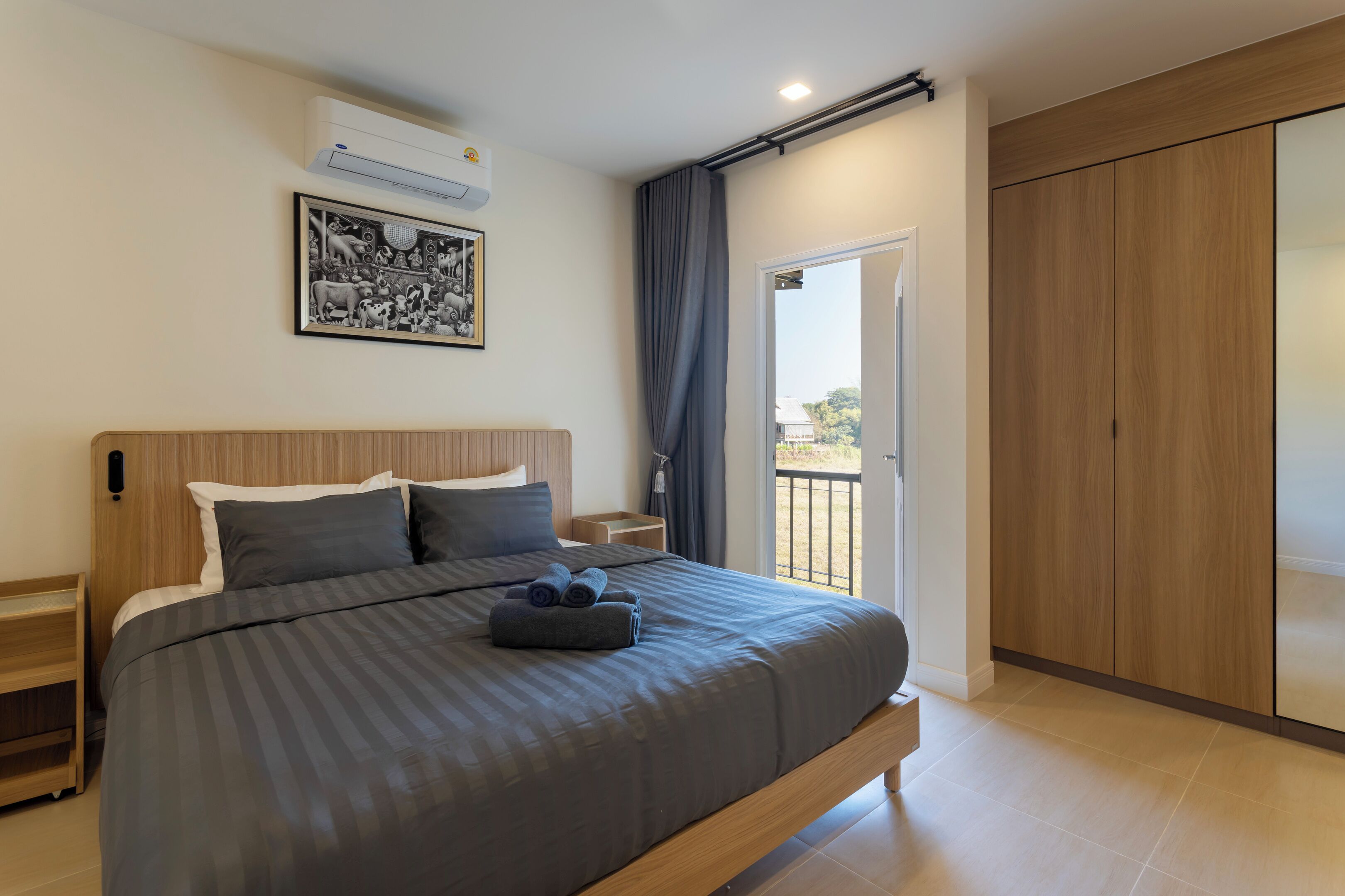 Un dormitorio moderno con una cama grande, una mesita de noche, aire acondicionado instalado en la pared, un cuadro enmarcado y una puerta corrediza a un balcón.
