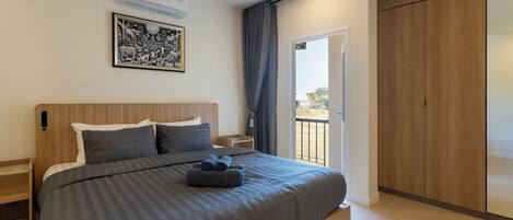 Un dormitorio moderno con una cama grande, una mesita de noche, aire acondicionado instalado en la pared, un cuadro enmarcado y una puerta corrediza a un balcón.