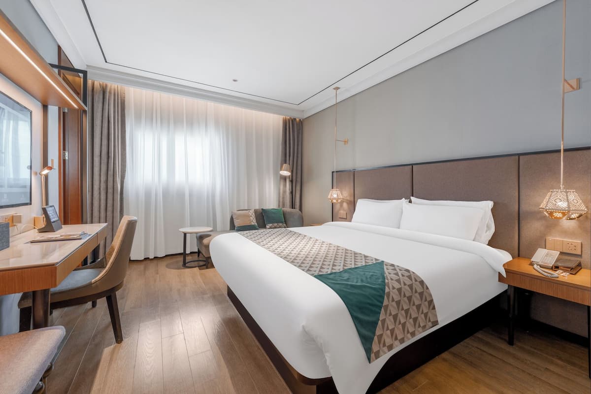 A modern hotel room with a large bed, a desk, a chair, and a small table.