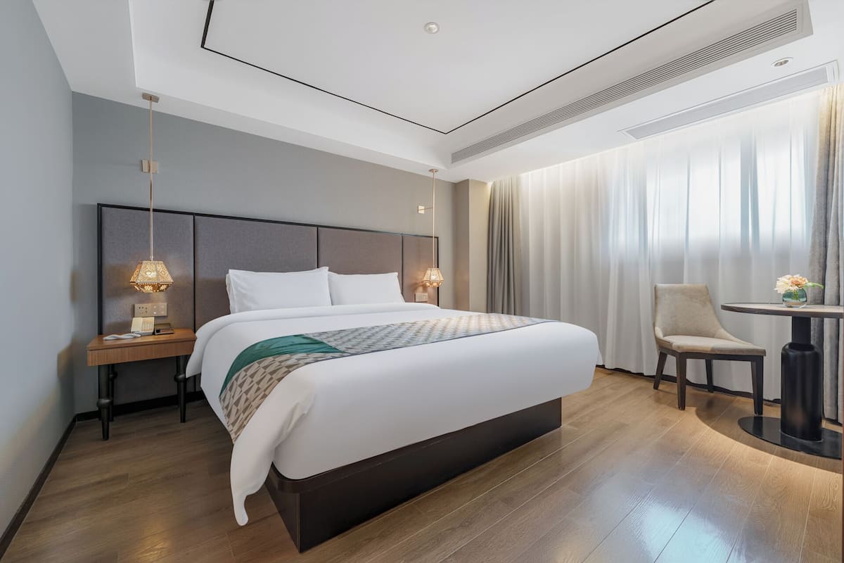 A modern hotel room with a large bed, bedside lamps, a small table with a vase, and a chair.