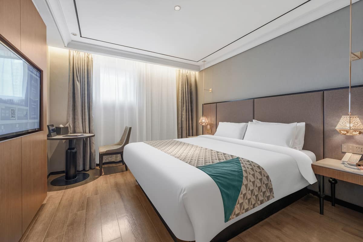 A hotel room with a large bed, a desk, a chair, a TV, and a window with curtains.