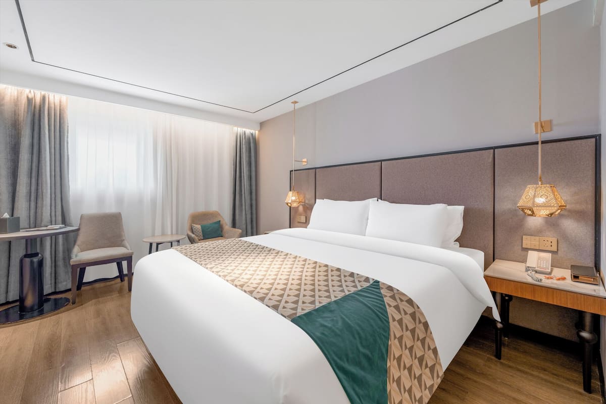 A hotel room with a large bed, a desk, a chair, and a nightstand.