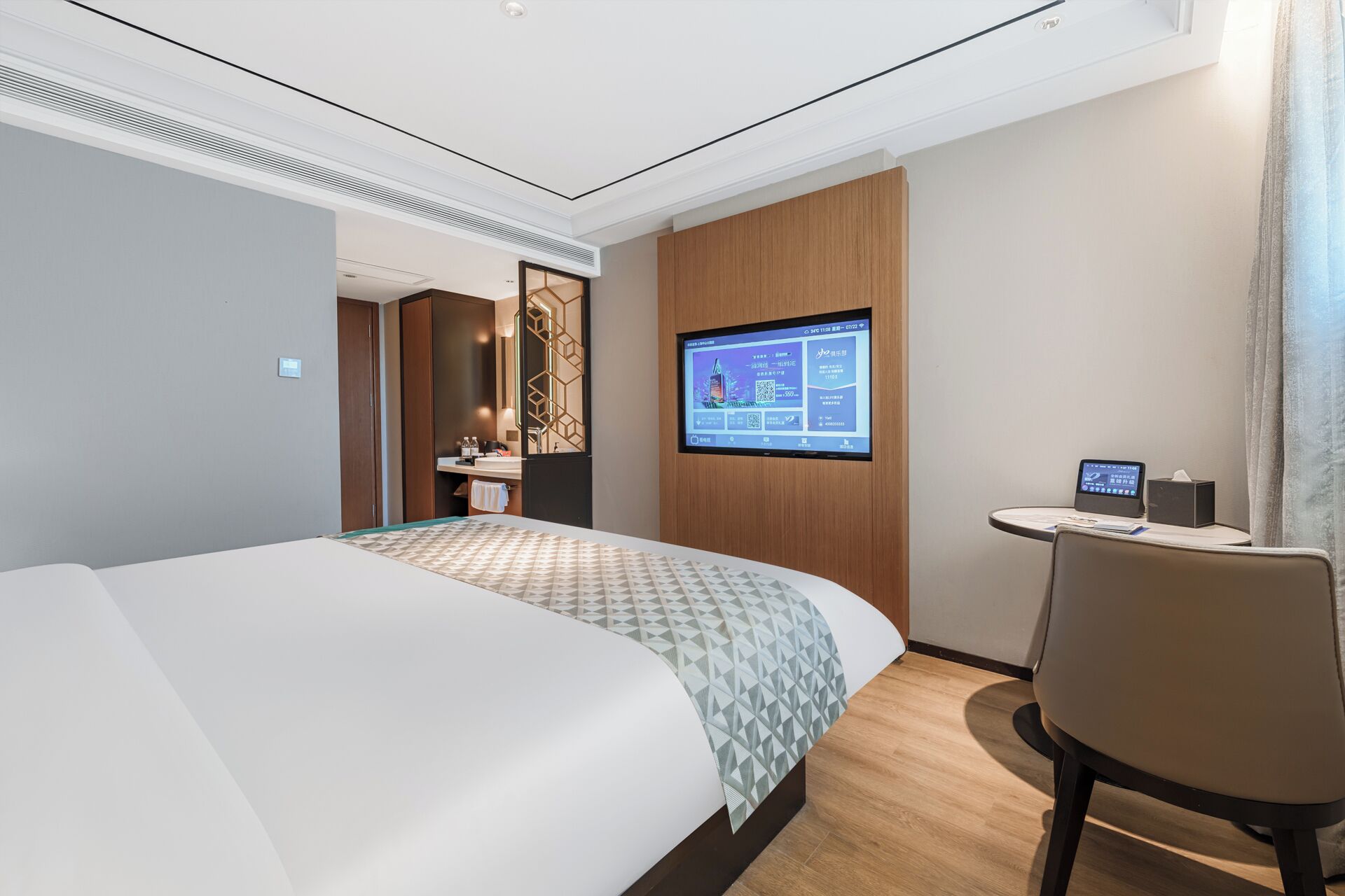 Ein Hotelzimmer mit Bett, Schreibtisch, Stuhl, Fernseher und einem Badezimmer mit Spiegel und Waschbecken.