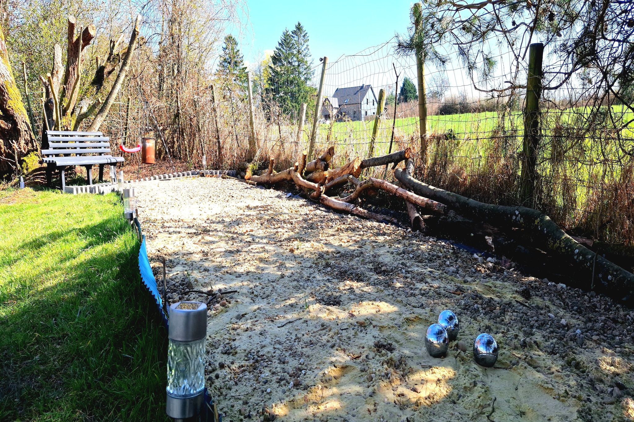 A dirt path with a bench, a fence, and a house in the background.