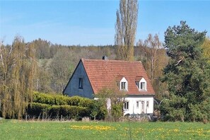 Una casa de dos pisos con techo rojo y paredes blancas, rodeada por un campo cubierto de hierba y árboles.