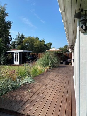 A wooden deck with potted plants, a small shed, and a patio umbrella.