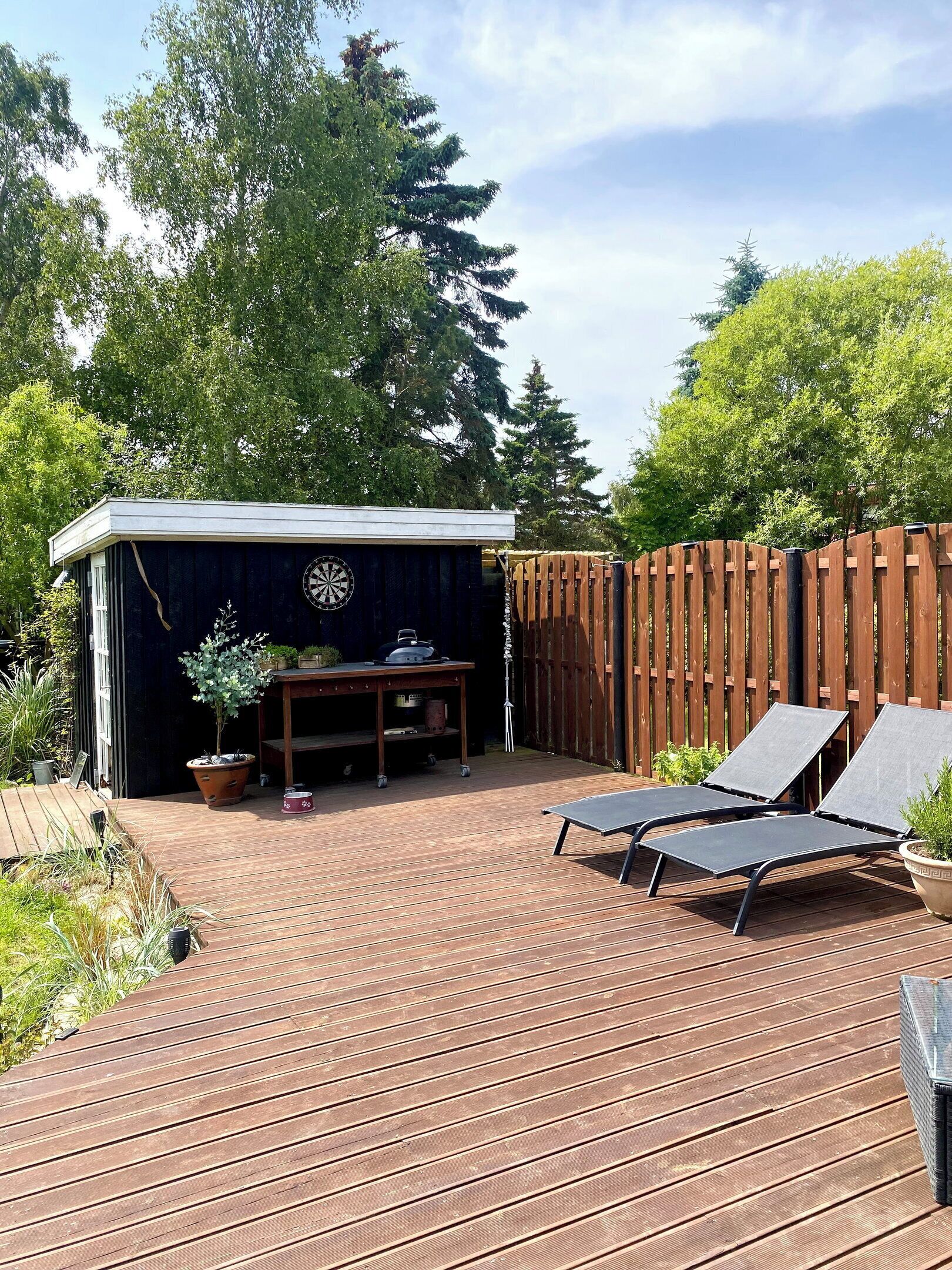 A wooden deck with lounge chairs, a barbecue grill, and a shed with a clock.