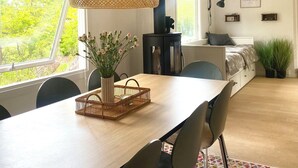 Ett modernt matområde med ett träbord, stolar, en flätad hänglampa och utsikt över grönskan utanför.