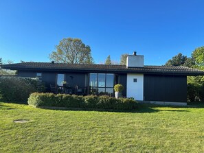 Una casa moderna de un piso con techo plano, ventanas amplias y un pequeño porche.