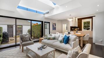 A modern living room with a large sofa, a coffee table, and a dining area with a wooden table and chairs.