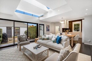 A modern living room with a large sofa, a coffee table, and a dining area with a wooden table and chairs. - Beautiful home in Sandy Bay (Sandy Bay)