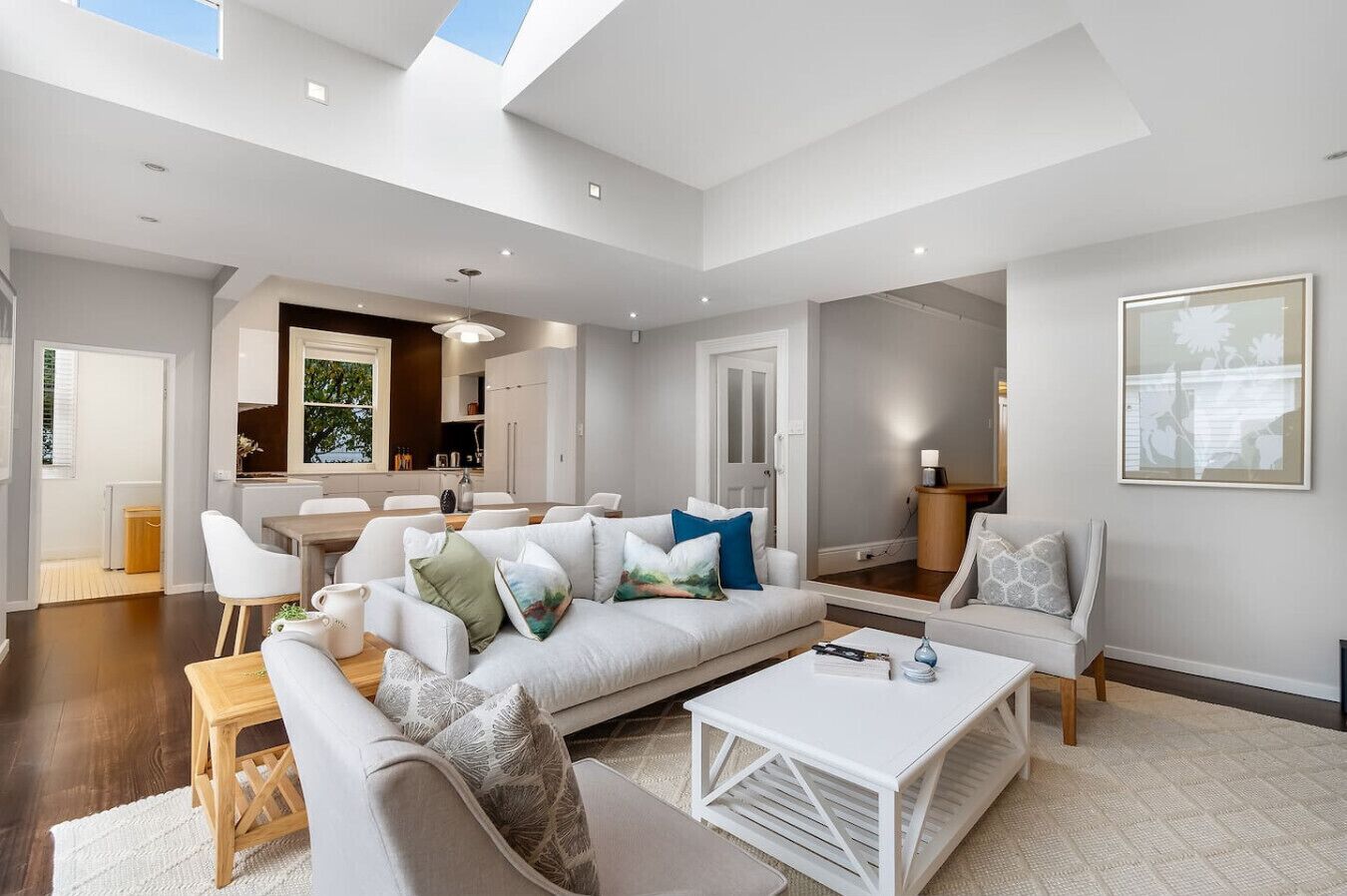 A modern living room with a sofa, coffee table, and chairs. There is a kitchen area with cabinets and a dining table.