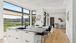 Une cuisine moderne dotée d’un grand îlot central, de grandes fenêtres et offrant une vue sur l’extérieur.