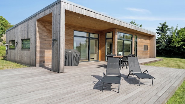 Une maison moderne dotée d’une terrasse en bois, de grandes fenêtres et d’un espace salon extérieur.