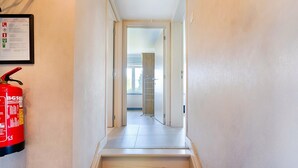 Un couloir étroit, avec un extincteur fixé au mur, qui mène à une pièce dotée d’une porte et d’une fenêtre.