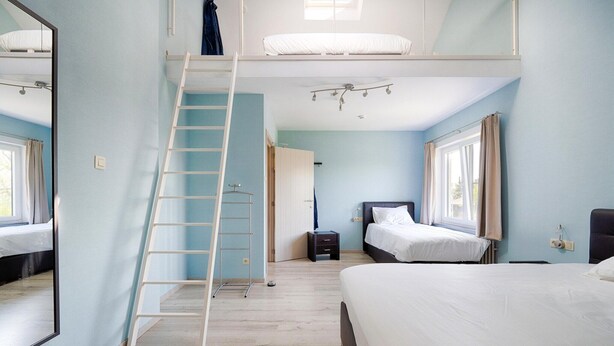 Une chambre avec un lit superposé, une échelle, une table de chevet et une fenêtre.