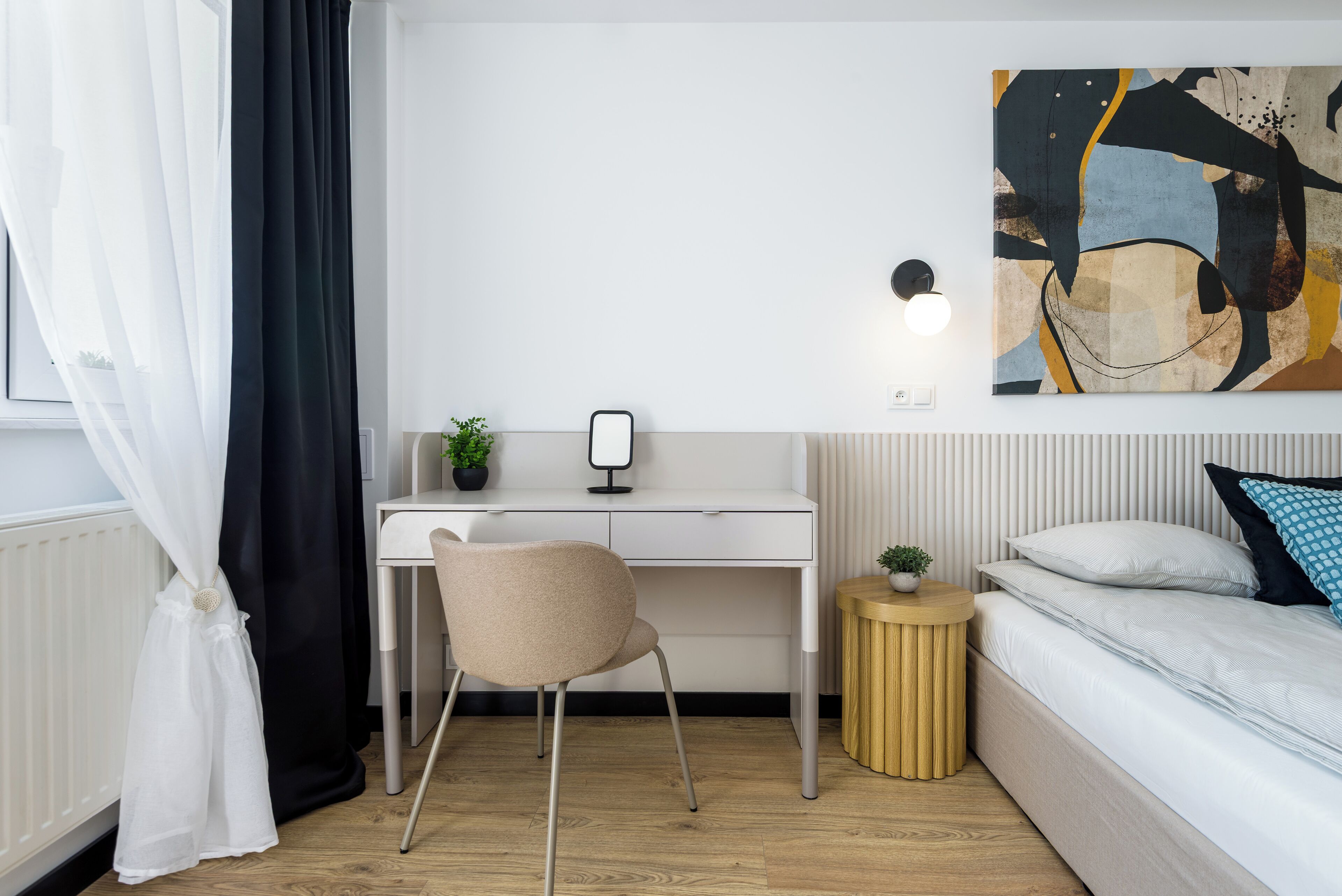 A modern bedroom with a bed, a desk, a chair, and a bedside table with a lamp.