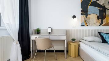A modern bedroom with a bed, a desk, a chair, and a bedside table with a lamp.