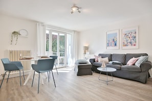 Un salon moderne avec un canapé gris, des fauteuils bleus, une petite table ronde et un coin repas comprenant une table et des chaises blanches.