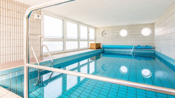 A swimming pool with clear blue tiles, a metal ladder, and a windowed wall. - Lornsen-Hof, App. 2 - Modern apartment on the ground floor with 2 rooms on approx. 50 m², (Sylt)