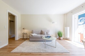 Uma sala de estar com sofá, mesa de centro, abajur e um vaso de planta.