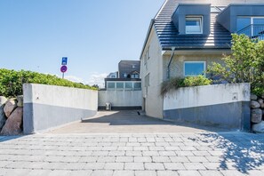 Een modern gebouw met een verharde opgang, een parkeersbord en een betonnen afscheiding.