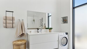 Une salle de bain moderne avec un meuble-lavabo blanc, un lave-linge, un porte-serviettes suspendu et une petite étagère ornée d’objets décoratifs.