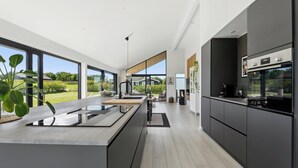 Une cuisine moderne dotée de grandes fenêtres, d’un îlot central et offrant une vue sur l’extérieur.