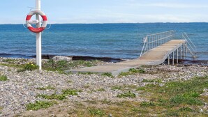 Une jetée en bois menant à une côte rocheuse, avec une bouée de sauvetage fixée à un poteau.