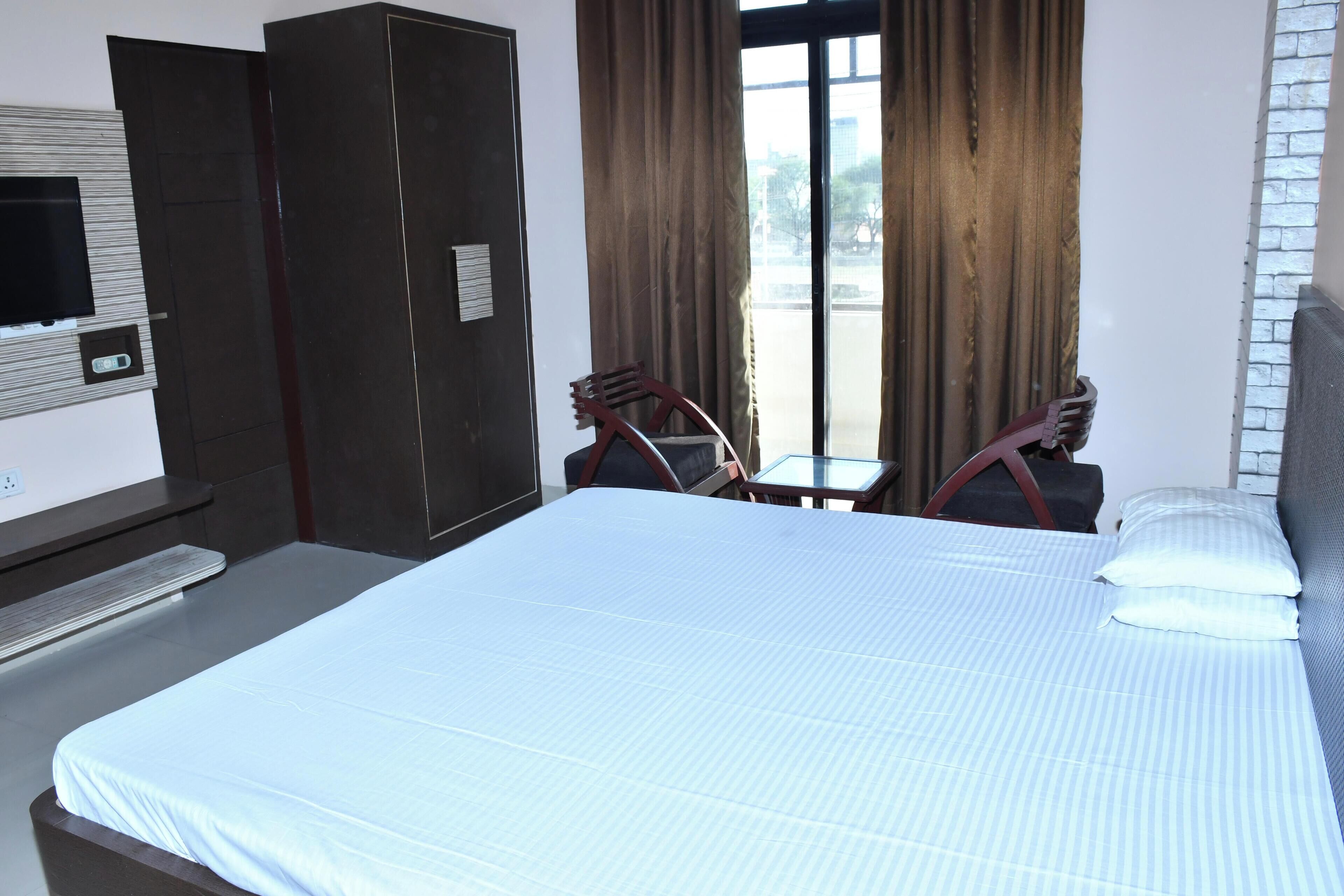 A hotel room with a large bed, a TV, a wardrobe, and a view of the outdoors through a window.