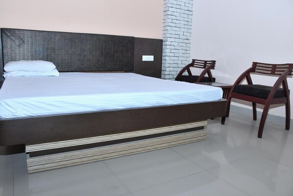 A neatly made bed with a headboard, two wooden chairs, and a small table.