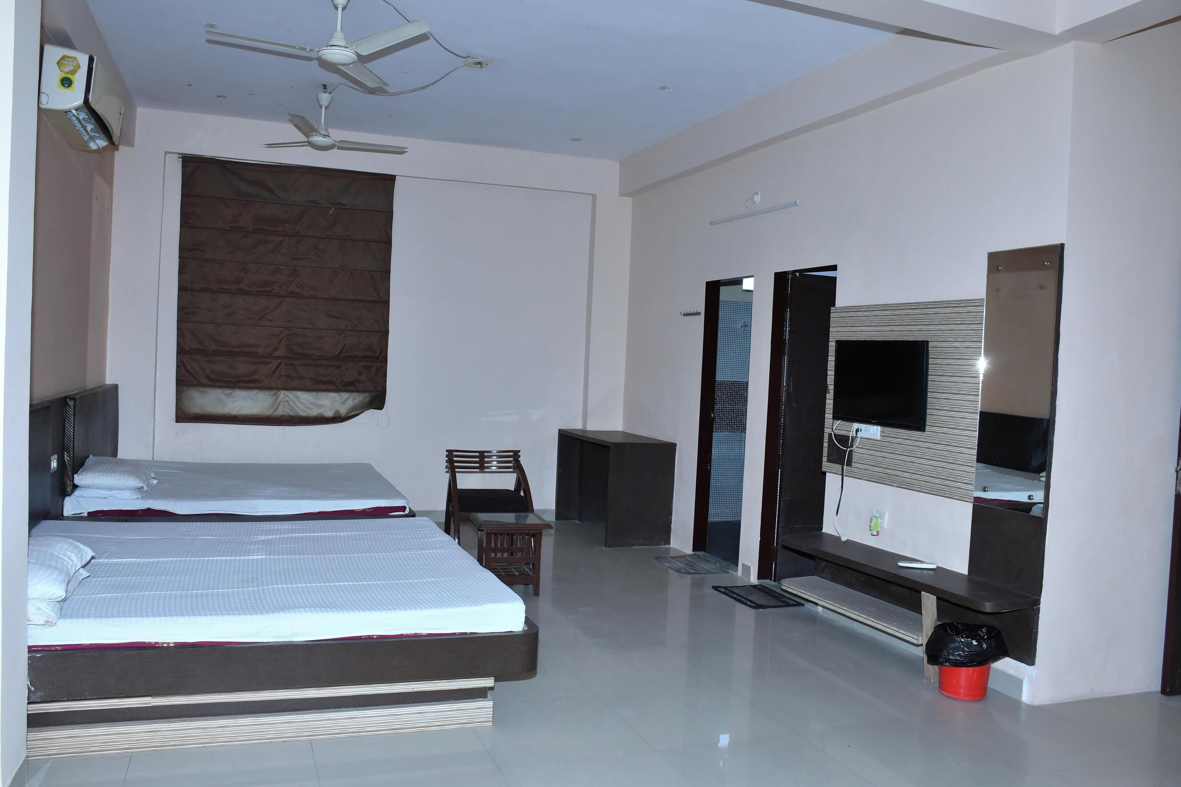 A modern hotel room with two beds, a TV, a ceiling fan, and a large window with blinds.